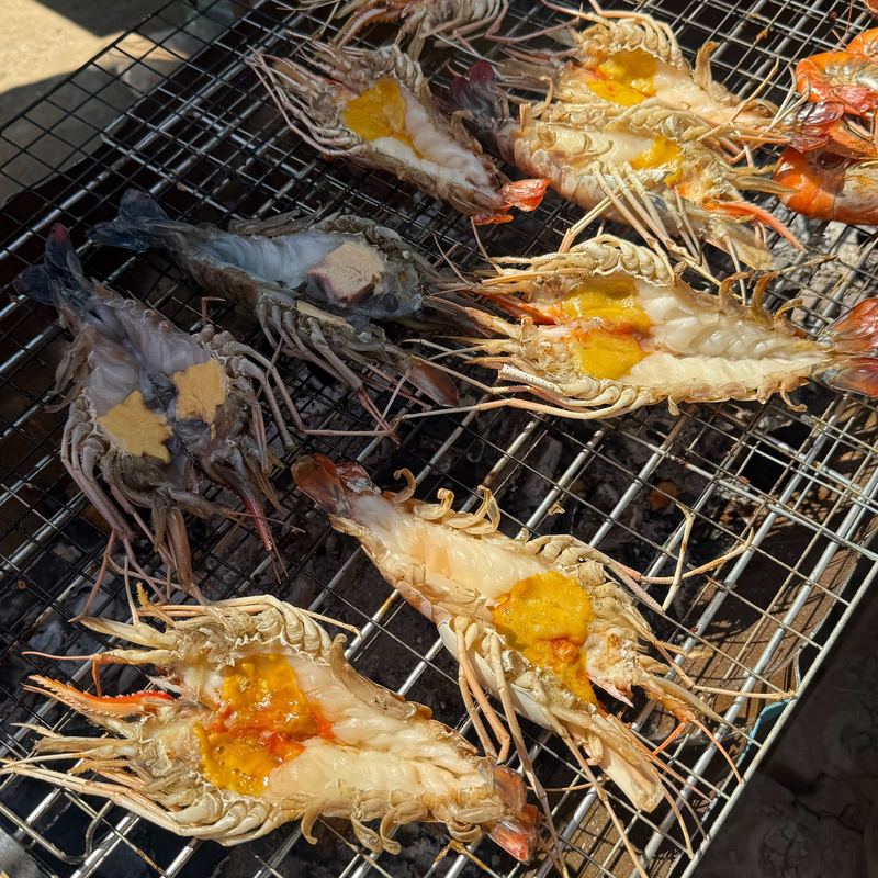 กุ้งแม่น้ำผ่าครึ่งวางย่างบนตะแกรง มันกุ้งสีส้ม